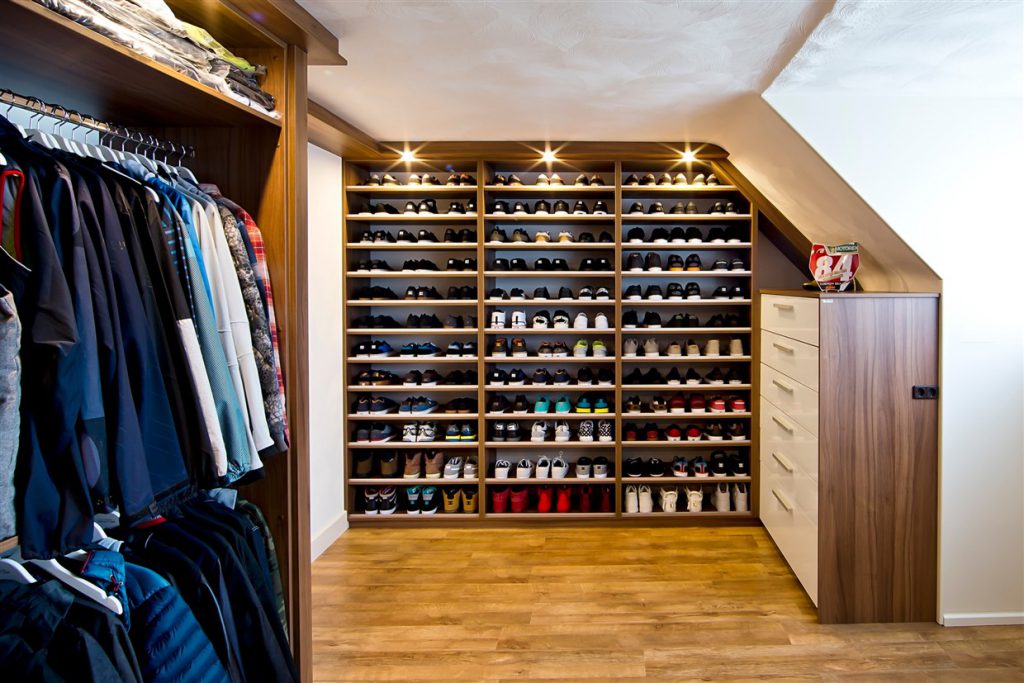 inloopkast met houten vloer en inbouwkasten gevuld met kleren en schoenen
